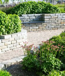 Moderner Garten- und Landschaftsbau: Gehweg und Mauern aus Natursteinen mit integrierten Sitzbänken und Anpflanzungen